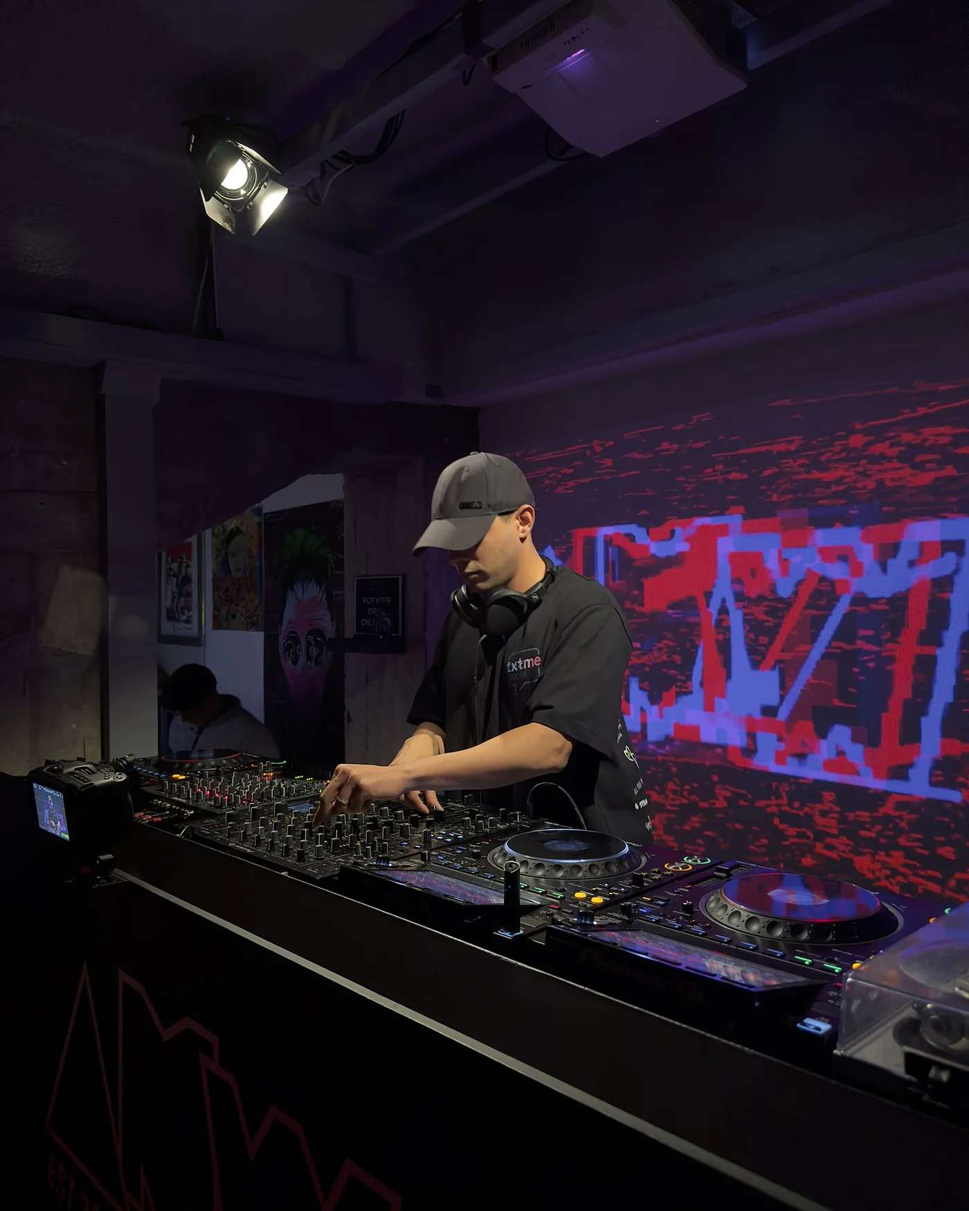 The DJ at the decks, cap pulled low